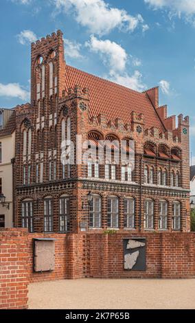 Deutschland, Wismar - 13. Juli 2022: Nahaufnahme von rotem Backstein mit schwarzen und beigen Zierleisten Archidakonat oder Archdeakonat Haus unter blauer Wolkenlandschaft. Lang hoch Stockfoto