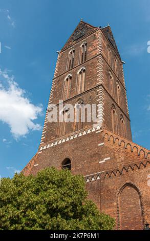 Deutschland, Wismar - 13. Juli 2022: Rückseite von St.. Marienkirchturm, St. Mary Kirchturm, während des Zweiten Weltkriegs als Denkmal unter blauer Wolkenlandschaft beschädigt, rot br Stockfoto