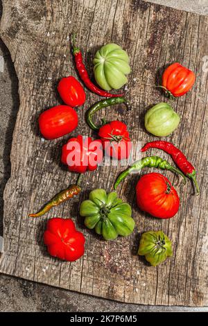 Grüne und rote gerippte Tomaten auf einem alten Holzständer. Amerikanische oder florentinische Sorte. Ein trendiger harter, dunkler Schatten, Steinbeton-Hintergrund, Stockfoto