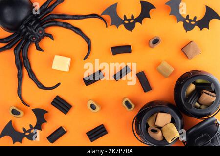 Auf einem orangen Hintergrund, die Komposition zu Halloween. Eine Spinne sitzt in der Ecke, es gibt Süßigkeiten um, in einer anderen Ecke der Süßigkeiten liegen in SM Stockfoto