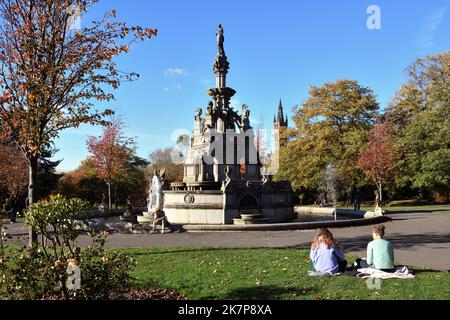 Der Stewart Memorial Fountain im Kelvingrove Park, Glasgow, Schottland, ist ein beliebter Ort für Studenten (Turm hinten), um in den Sonnen zu studieren Stockfoto