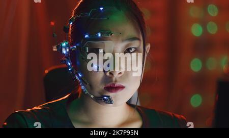 Asiatisches Mädchen im Cyberpunk-Stil trägt eine Augenbrille und ein Mikrofon mit kleinen LED-Leuchten blickt mit ernstem Gesichtsausdruck auf die Kamera. Sci-Fi-Hintergrund mit Neonlicht. Stockfoto