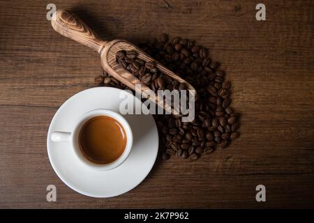 Geröstete Kaffeebohnen mit einer Tasse Espresso auf einem Holztisch Stockfoto