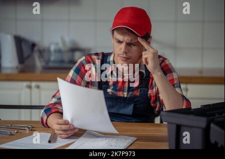 Fokussierter, in Arbeitskleidung gekleideter Servicetechniker, der die Installationsanweisungen durcharbeitet Stockfoto