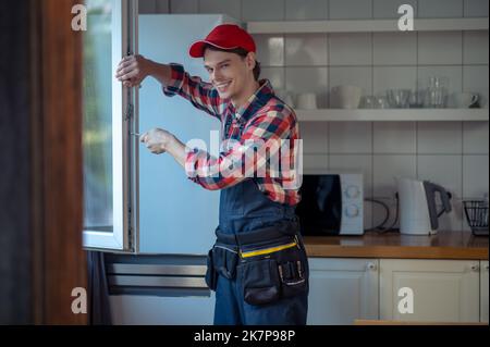 Zufrieden junger Reparaturmann, der das Fenster in einer Kundenküche installiert hat Stockfoto