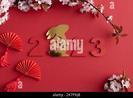 Chinesisches Neujahr, Jahr des Kaninchens. Jahr 2023 mit goldenen Hasen und Papier ausgeschnittenen Ventilatoren mit natürlichen Pflaumenblüten. Speicherplatz kopieren. Draufsicht. Stockfoto