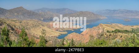 Landschaftspanorama des Nurek-Staudamms, zweithöchster See der Welt zwischen den Regionen Duschanbe und Khatlon in Tadschikistan, mit Bäumen im Vordergrund Stockfoto