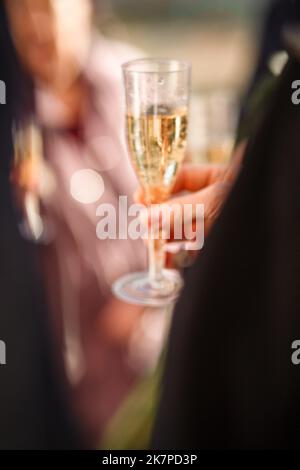 Silvester verschwommen festlichen Hintergrund mit einem Mann die Hand mit einem Glas Champagner und Bokeh aus Feuerwerk. Hochzeit Champagner-Party. Der Bräutigam in einem su Stockfoto