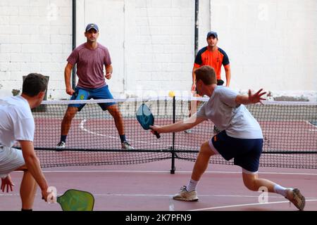 Eine Gruppe von weißen männlichen Millennials spielen in Manhattan, New York City, auf einem Basketballplatz mit zweifachem Pickleball und Basketballfeld-Striping Pickleball Stockfoto