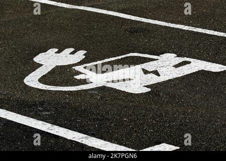 Ein Parkplatz, der für das Aufladen von Elektrofahrzeugen markiert ist. Das Schild auf dem Asphalt zeigt, dass der Platz für ein Elektrofahrzeug zum Laden und Parken ist. Stockfoto