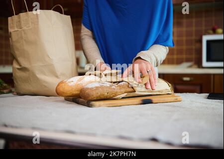 Nahaufnahme der Hände der Frau auf den Broten aus Sauerteig Vollkornbrot, während sie den Lebensmittelbeutel in der Küche zu Hause auspacken Stockfoto