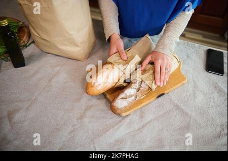 Draufsicht Frauenhand an Baguettes aus Sauerteig-Vollkornbrot beim Auspacken des Lebensmittelbeutels in der Küche zu Hause Stockfoto
