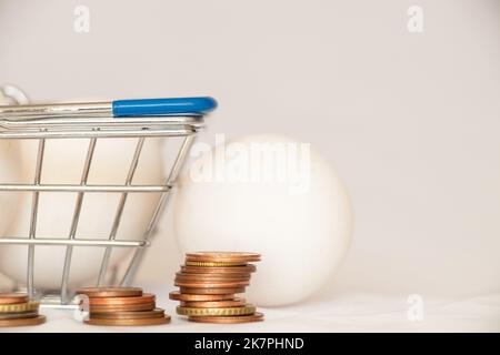 Hühnereier in einem Korb aus einem Supermarkt und ein Stapel von Münzen auf weißem Hintergrund, der Preis für Eier im Laden Stockfoto