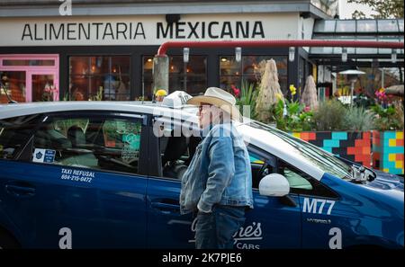 Reifer männlicher Taxifahrer in der Nähe des Autos. Mann mit Hut, der sich an einem Taxistand lehnte, der auf einer belebten Straße in Vancouver, BC, Kanada, geparkt war. Reisefoto, selektive fo Stockfoto