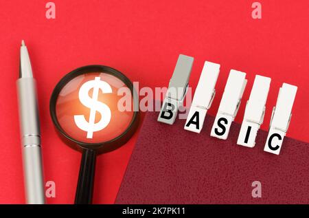 Geschäftskonzept. Auf der roten Oberfläche befindet sich ein Stift, eine Lupe mit einem Dollarsymbol und ein Notizblock mit Wäscheklammern und der Aufschrift - BASIC Stockfoto