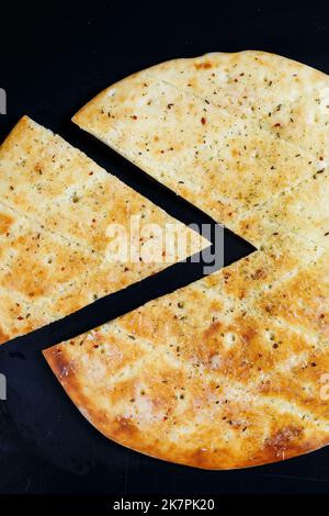 Pizza in Scheiben auf schwarzem Stein, Draufsicht. Frisch gebackene Focaccia mit Käse Stockfoto