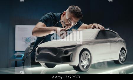 Senior Car Designer und Entwickler arbeitet an einem Prototyp einer Autoskulptur aus Lehm. Die letzten Nachbearbeitungen mit dem geponierten Ende der Fräsmaschine durchführen. Ein innovatives High-Tech-Büro. Stockfoto