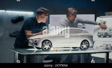 Zwei erfahrene Automobilingenieure diskutieren das Fahrzeugdesign anhand der Skizzen auf dem Brett. Korrekturen an der Prototyp-Rechen-Skulptur mit einem rotierenden Werkzeug mit drehender Spitze. Stockfoto