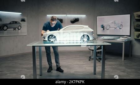 Ein Automobilingenieur und -Designer arbeitet in einem modernen Studio mit heller LED eines Automobilkonzerns an einem Prototyp-Modellauto. Konstruktionskorrekturen Vornehmen. Stockfoto