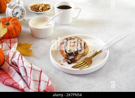 Hausgemachte Kürbis-Zimtrollen mit Frischkäse auf dem Teller. Saisonales hausgemachtes Gebäck im Herbst - Zimtgebäck zum Frühstück oder für den Urlaub. Stockfoto