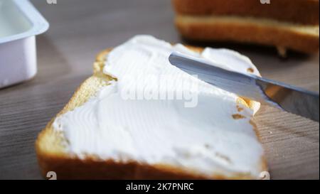 Messer, Butter auf einem Stück Brot verteilen, Nahaufnahme. Frühstück oder Mittagessen Stockfoto