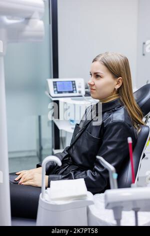 Eine junge Frau sitzt in einem Zahnarztstuhl. Zahnschmerzen. Warten auf Zahnbehandlung. Zahnarztpraxis Stockfoto