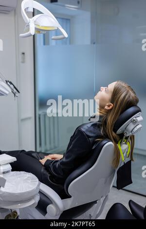 Eine junge Frau sitzt in einem Zahnarztstuhl. Zahnschmerzen. Warten auf Zahnbehandlung. Zahnarztpraxis Stockfoto