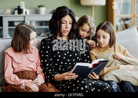 Porträt einer jungen jüdischen Mutter, die zu Hause drei Mädchen ein Buch liest Stockfoto
