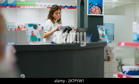 Apothekerin scannt Medikamentenboxen an der Drogerietheke und hilft Kunden, pharmazeutische Produkte und Pillen zu kaufen. Mitarbeiter, der am Apothekenschalter mit Zuschlägen arbeitet. Stockfoto