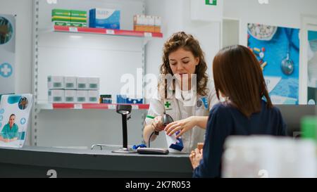 Medizinischer Mitarbeiter, der Kunden mit Pillen und Medikamenten versorgt, Medizinprodukte scannt und in der Apotheke Hilfe leistet. Apotheker hilft Menschen, Behandlung und Medikamente zu kaufen. Handgeführte Aufnahme. Stockfoto
