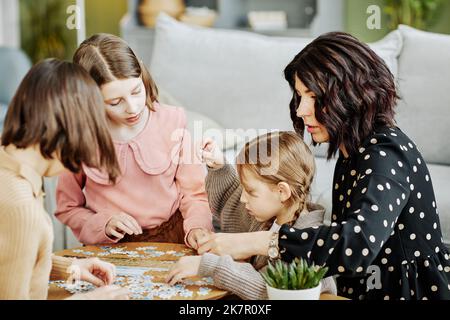 Seitenansicht Porträt einer jungen Mutter mit drei Kindern, die zusammen mit Puzzle in der häuslichen Umgebung spielen Stockfoto