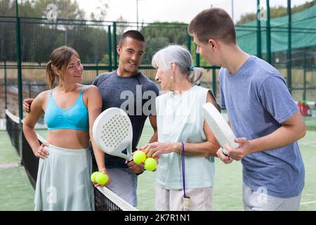 Glückliche Spieler mit Schlägern für Padel, die auf dem Tennisplatz im Freien reden Stockfoto