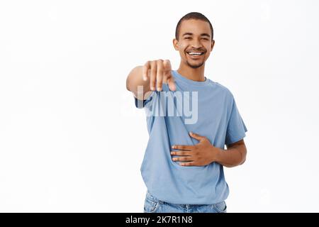 Haha lustig. Lachend und lächelnd zeigt der Mann mit dem Finger auf die Kamera, siehe smth urkomisch, steht auf weißem Hintergrund Stockfoto