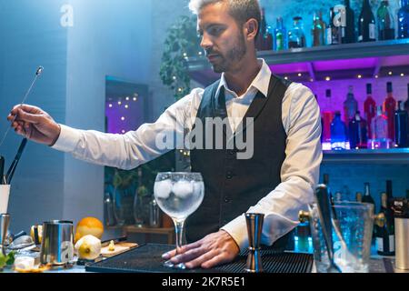 Barkeeper in einem weißen Hemd und schwarzer Schürze, der bei einer Party im Nachtclub Cocktails zubereitet. Nachtleben. Stockfoto