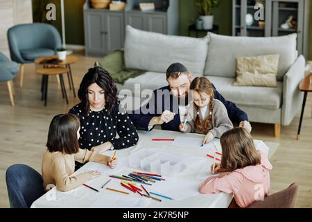 Hochwinkelporträt der jüdischen Familie, die sich zusammenzieht, während sie zu Hause mit drei Kindern am Tisch sitzt Stockfoto