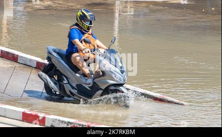 SAMUT PRAKAN, THAILAND, Okt 13 2022, Ein Motorradfahrer fährt mit den Füßen nach oben durch eine überflutete Straße Stockfoto