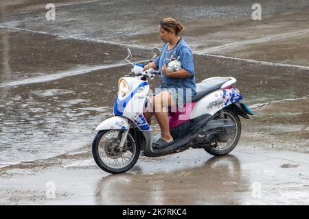 SAMUT PRAKAN, THAILAND, SEP 26 2022, Eine Frau mit Geld in Plastiktüte fährt bei starkem Regen ein Motorrad auf der Straße Stockfoto