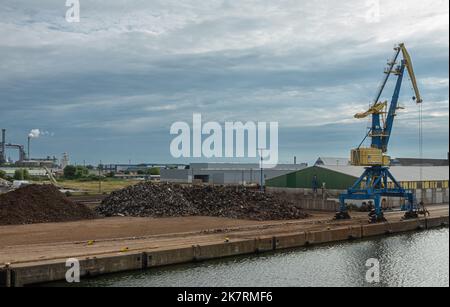 Deutschland, Wismar - 13. Juli 2022: Kran und entlang Norddock des Hafens mit Bahnterminal und Lagerhallen im Rücken. Haufen von Recyclingmaterialien auf Stockfoto