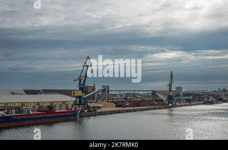 Deutschland, Wismar - 13. Juli 2022: 2 Krane entlang des Nordhafens mit Bahnterminal und Lagerhäusern. Schüttgutfrachter und Haufen von Recyclingmaterialien Stockfoto