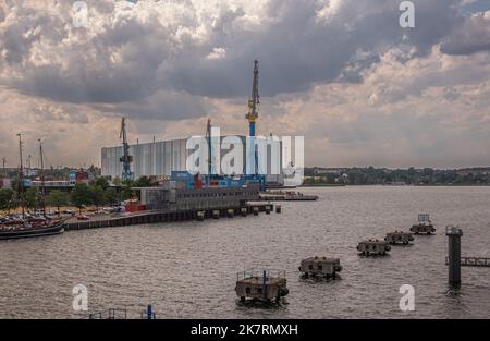 Deutschland, Wismar - 13. Juli 2022: Riesige weiße Schmidt Recycling-Verarbeitungsanlage hinter Kranen der Westhafen und Alter Holzhafen unter dicken Wolken Stockfoto