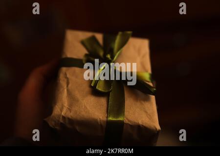 Defocus Craft Eco Geschenkbox mit magischem Licht vor dunklem, hellem Hintergrund. Dunkle Nacht. Handhaltung vorhanden. Nicht fokussiert Stockfoto