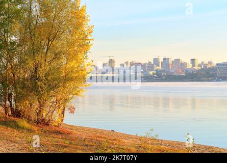 Nowosibirsk, Sibirien, Russland, 09.10.2022. Morgen am Ufer des ob. Herbstbäume am sandigen Ufer des Flusses, eine große Stadt in der Ferne Stockfoto