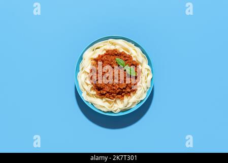 Draufsicht mit einem Teller Bolognese Pasta auf einem blauen Teller minimalistisch auf einem bunten Tisch. Köstliches italienisches Gericht, Tagliatelle mit Ragusauce. Stockfoto