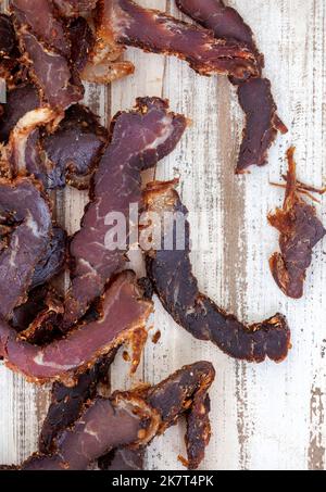 In Scheiben geschnittenes traditionelles südafrikanisches Biltong oder geräuchertes Fleisch auf rustikaler weißer Holzoberfläche Stockfoto