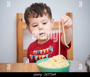 Netter Junge spielt mit seiner Pasta zur Mittagszeit Stockfoto
