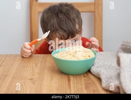 Netter Junge spielt mit seiner Pasta zur Mittagszeit Stockfoto