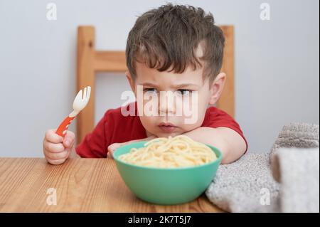 Netter Junge spielt mit seiner Pasta zur Mittagszeit Stockfoto