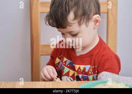 Netter Junge spielt mit seiner Pasta zur Mittagszeit Stockfoto