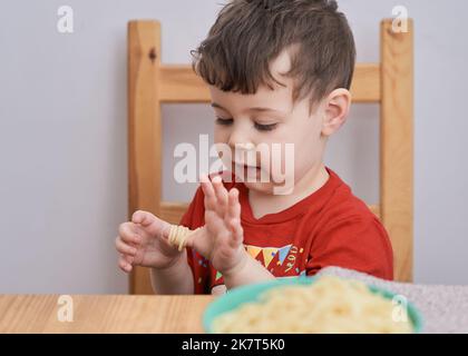 Netter Junge spielt mit seiner Pasta zur Mittagszeit Stockfoto
