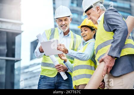 Einstellen der Zeitleiste auf Kurs. Eine Gruppe von Geschäftsleuten, die auf einer Baustelle ein digitales Tablet benutzen. Stockfoto